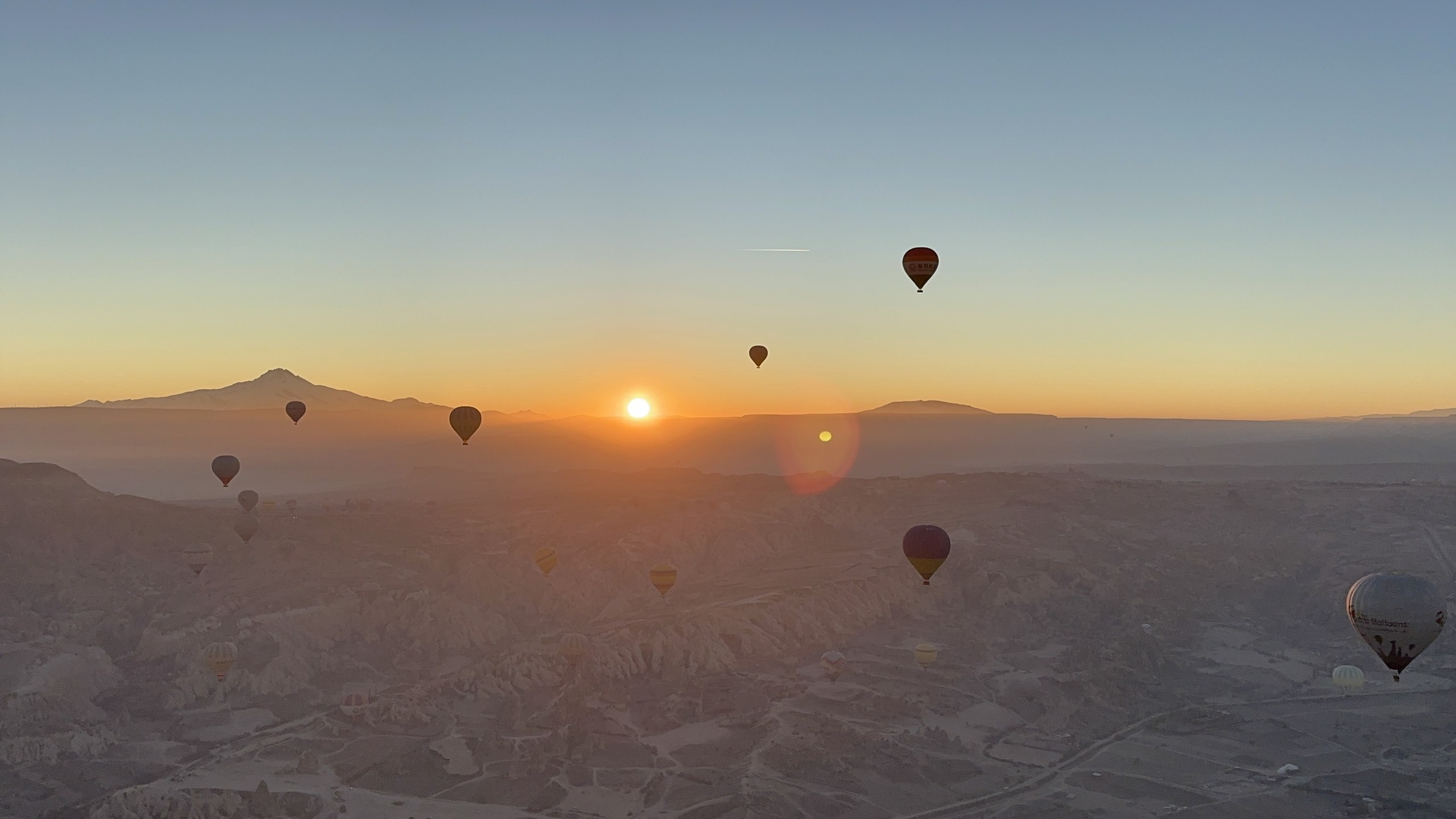 日の出の盛り：太陽、エルジェス山、気球のシルエットの群れが一つの画面に。谷は朝の光で輝く。