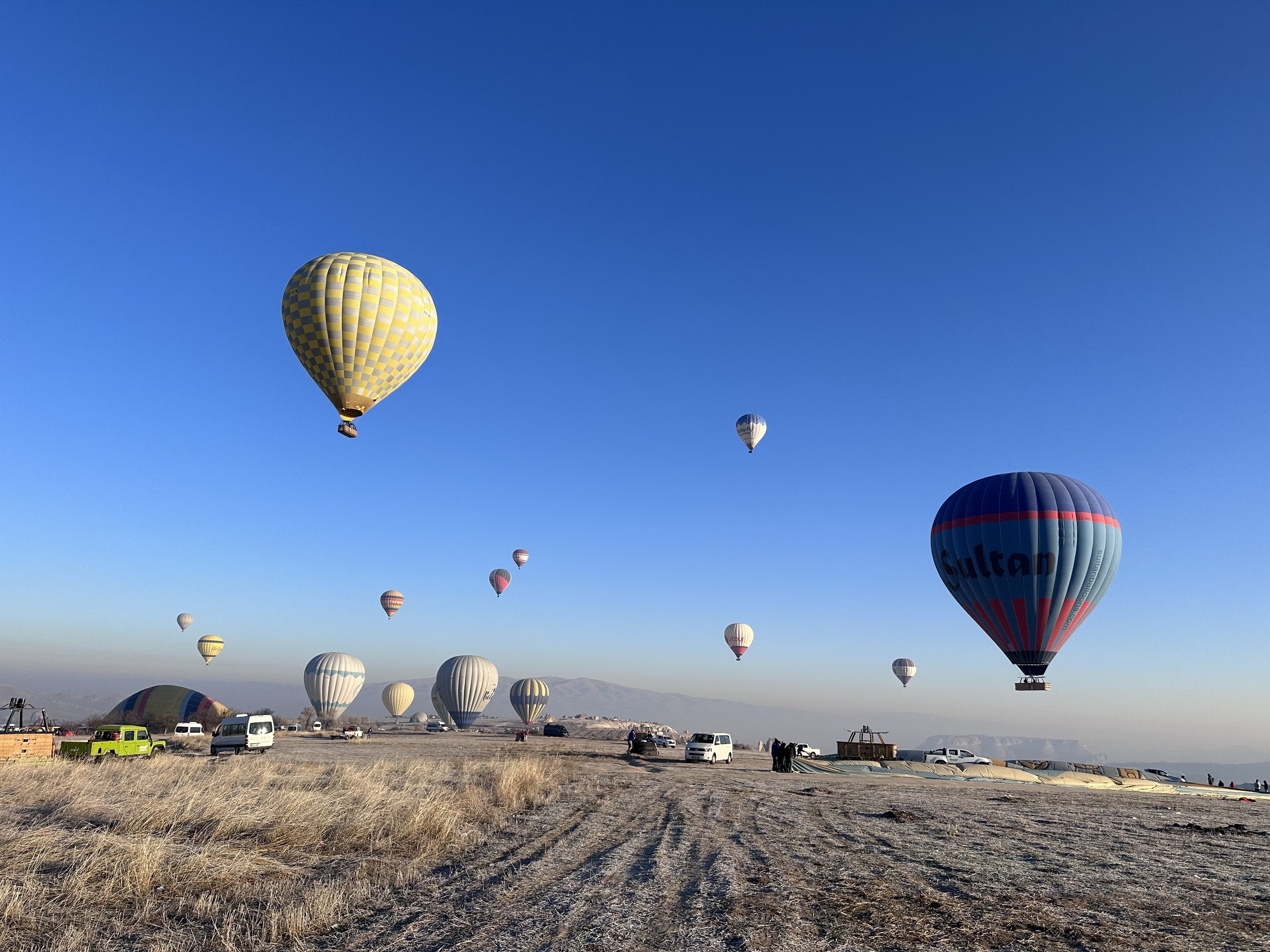 飛行を終えた着陸場の全景：空はすっかり明るく、気球が次々に降りる。地面には朝の霜と長い影。