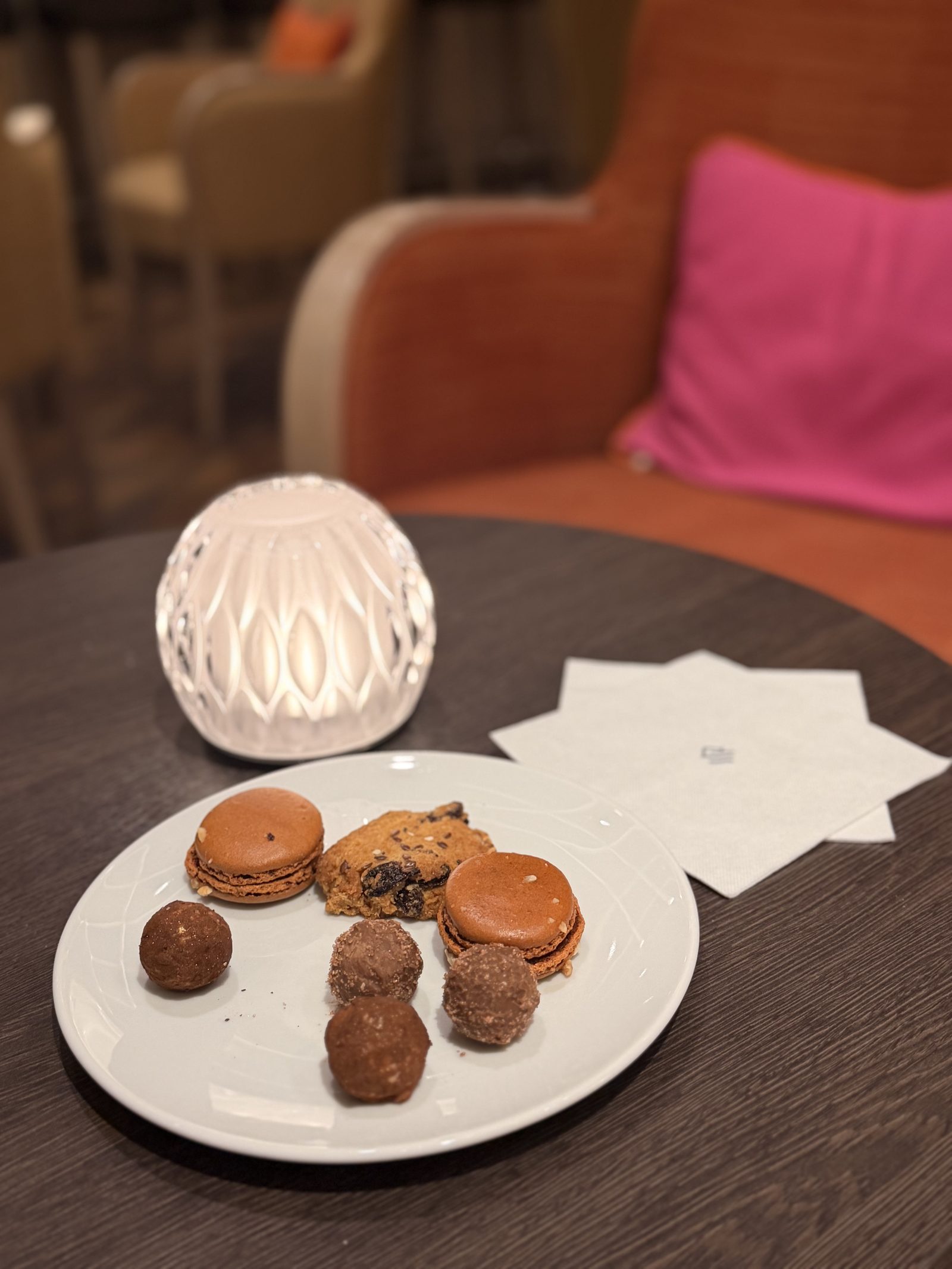 カフェのプチフール。マカロン2つ、チョコレートトリュフ4つとクッキー1枚。横にはカットガラスのランプ。