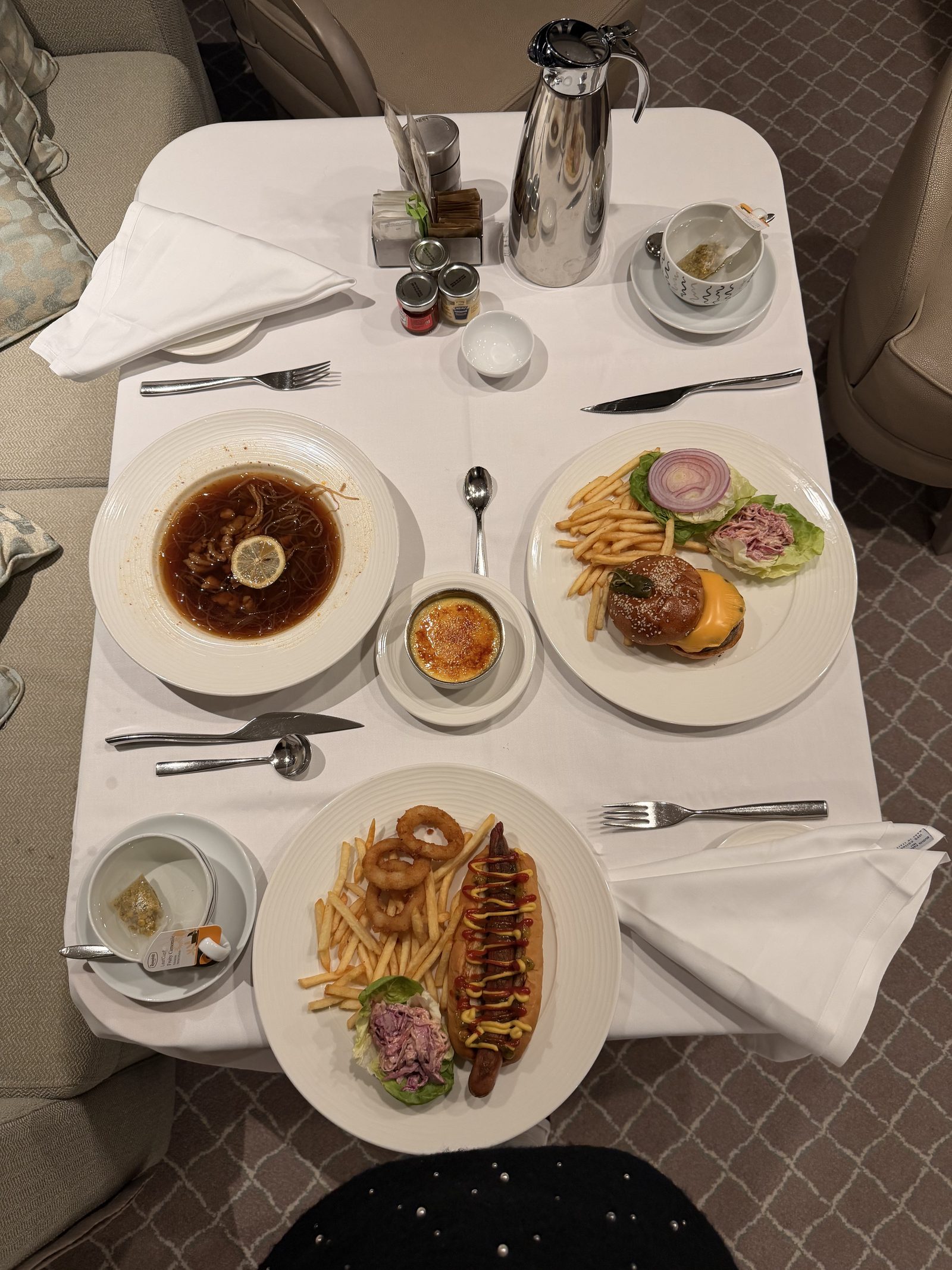 テーブルを上から。麺のスープ、チーズバーガー、ホットドッグ、クレームブリュレと温かいお茶2杯。