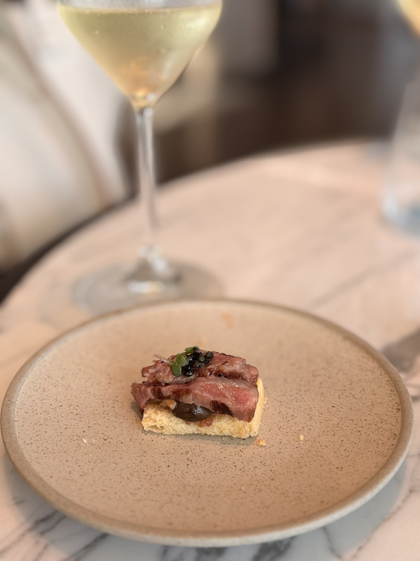 A single beef canapé, plated, with white wine.