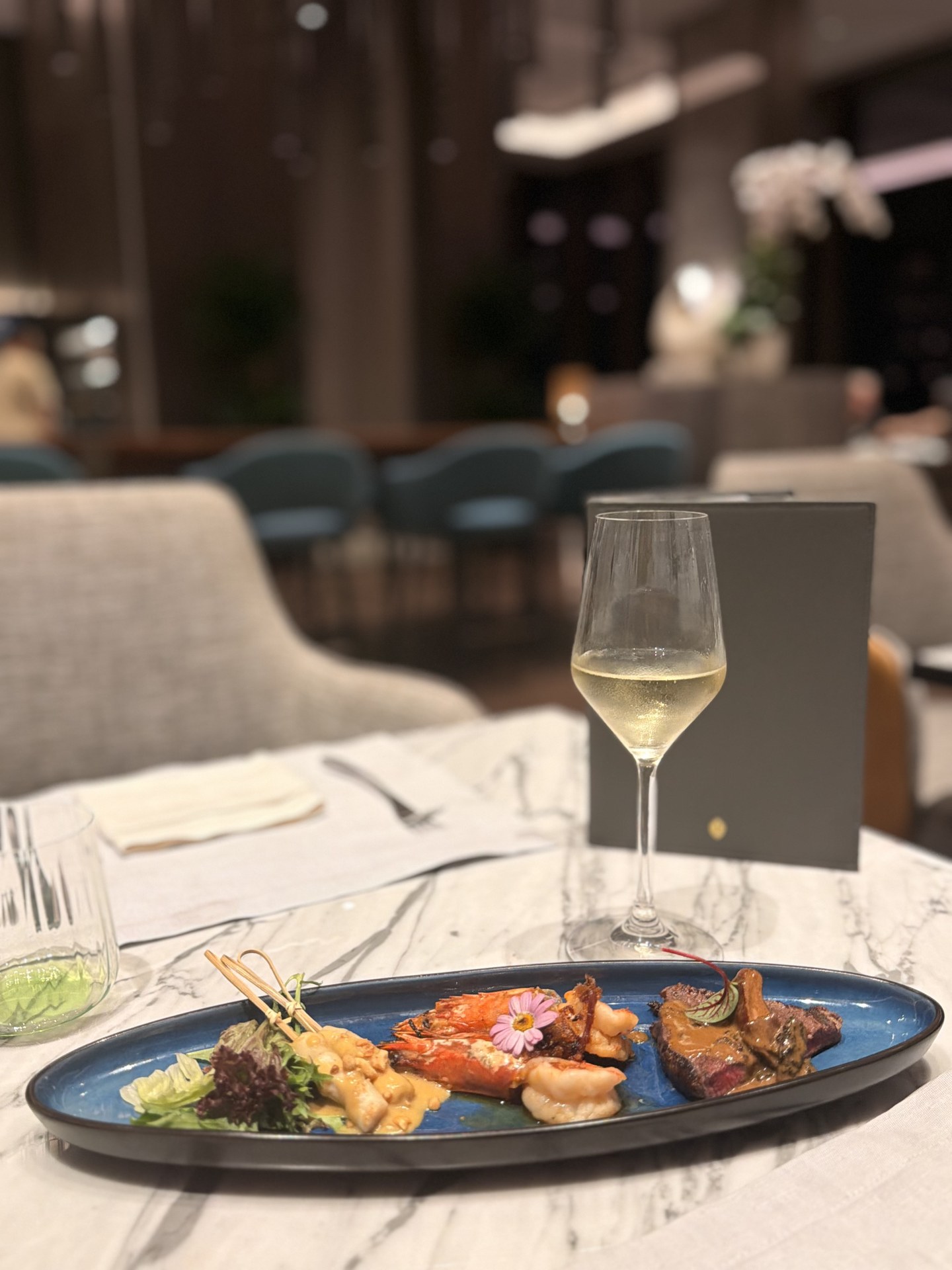 Long-plate hot dishes: skewers, prawns and beef, white wine alongside.
