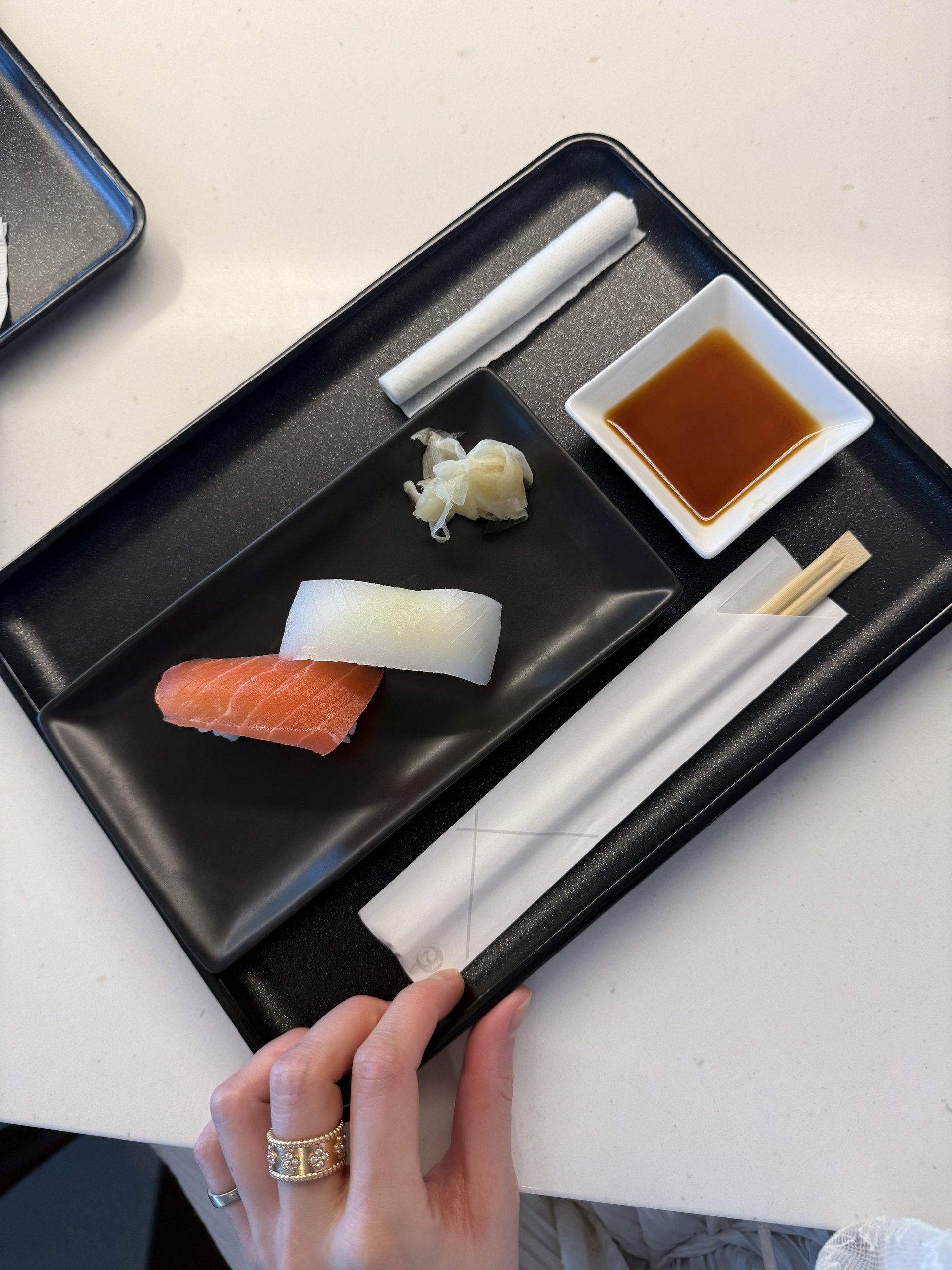 Back at the counter in the afternoon: two pieces made to order — salmon and cuttlefish — with ginger, soy and a JAL chopstick sleeve on the tray.